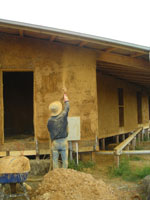 Second coat of render is applied to the straw bale walls using a pump.
